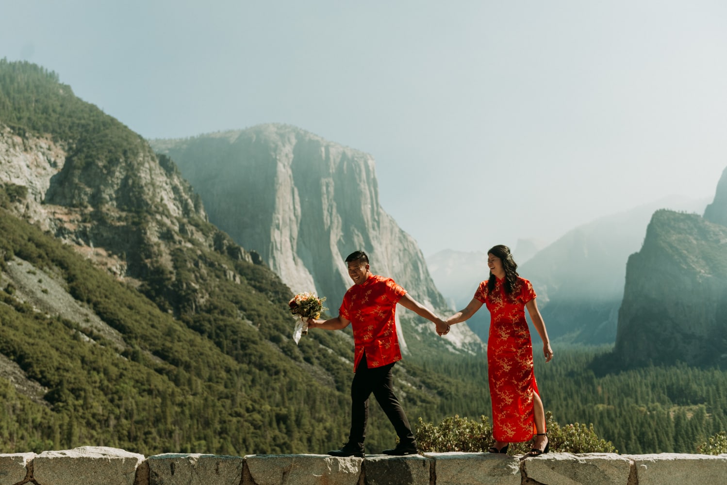 A couple in traditional chinese wedding attire walking on the rocks at tunnel view in Yosemite national park