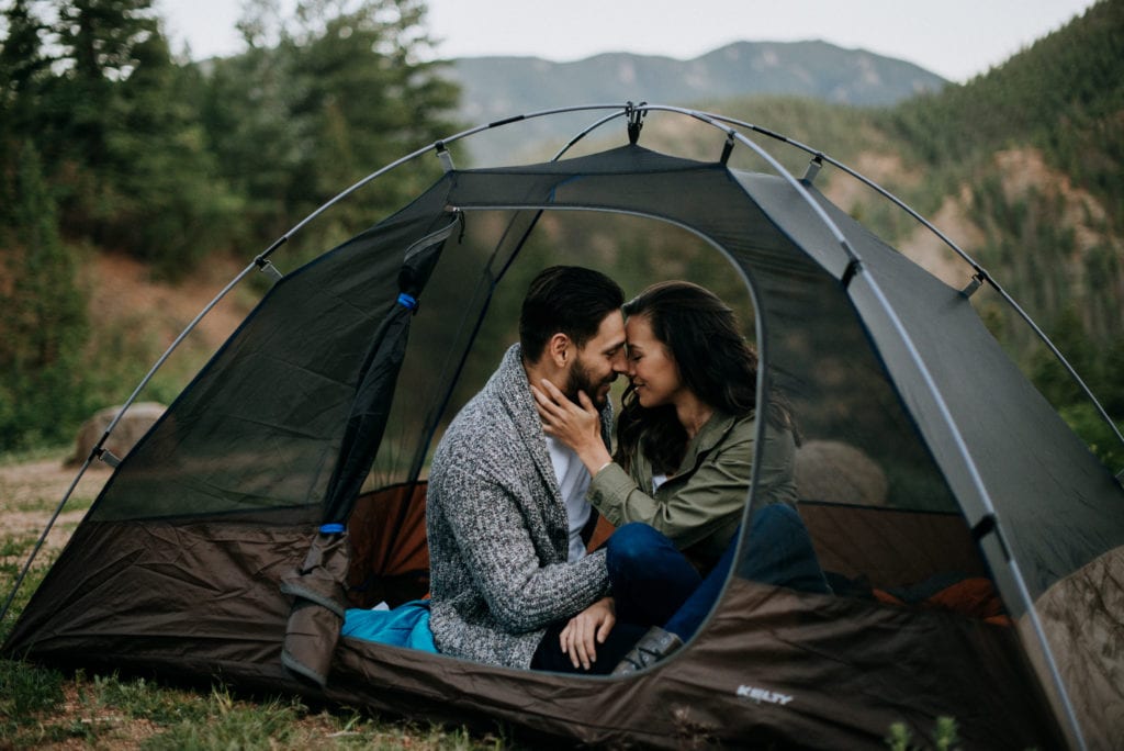 A couple snuggles up in their tent as the sun sets over the mountains in the background in Colorado Springs, Colorado. Camping is one of the best Colorado elopement ideas. 
