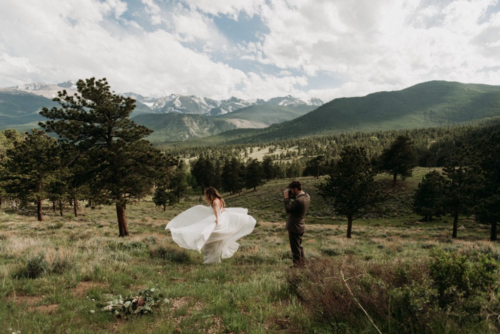 A couple dances in a meadow in front of a range of mountains in Rocky Mountain National Park during their elopement