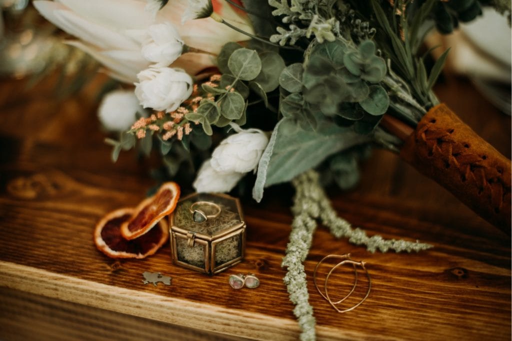 Detail shot of a handmade bridal bouquet with wedding rings, earrings and a gold ring box sitting on a table at the Wilds Venue in Bloomington, Indiana.