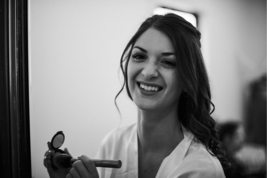 Black and white photos of a bride looking through the mirror at the camera and getting ready for her wedding ceremony at the Wilds Venue in Bloomington, Indiana in the bridal suite.