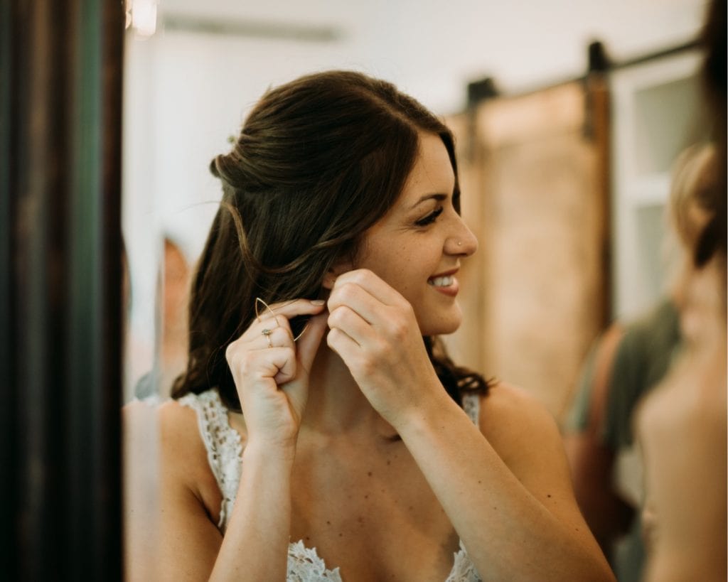 Bride putting her Katie Carder earrings in and getting ready for her wedding ceremony at the Wilds Venue in Bloomington, Indiana in the bridal suite.