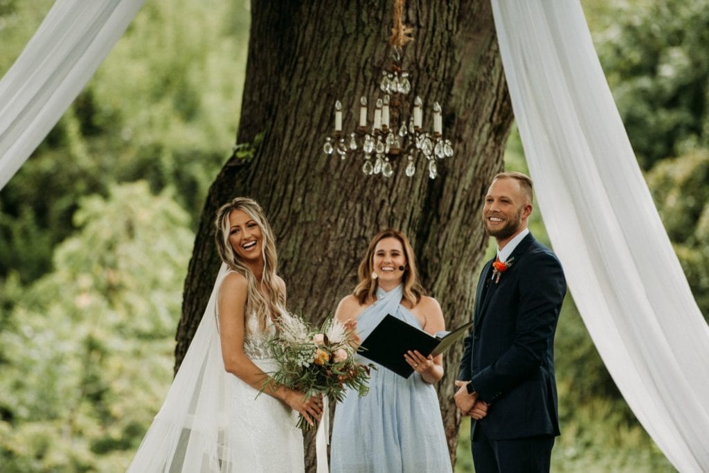 Bride and groom standing underneath a large oak tree during their boho summer wedding ceremony at Mustard Seed Gardens.