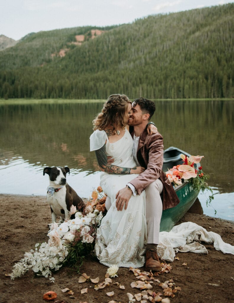 A couple sits on the edge of a canoe in their wedding attire on an alpine lake in Vail, Colorado at Piney River Ranch. Canoeing elopement ideas 