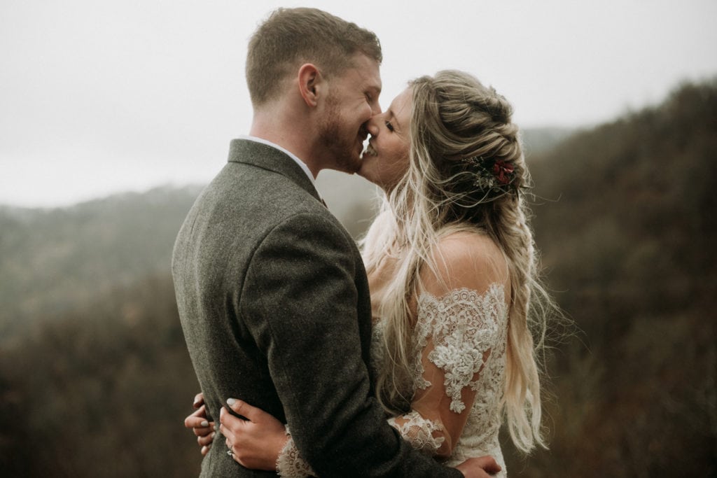 Wedding couple going in for a kiss with mountains in the background during their fun day of elopement ideas at Roan Mountain State Park in Tennessee. 