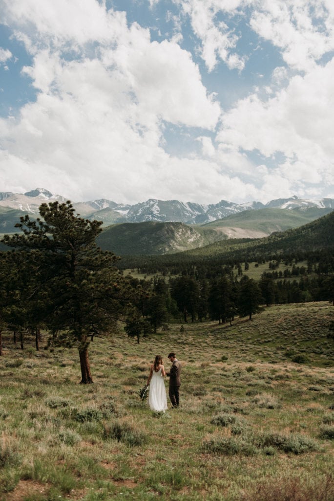 a couple walks towards a range of snow capped mountains in Rocky Mountain national park during their elopement day