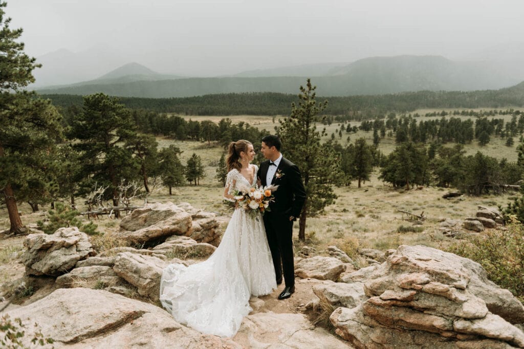 A couple looks at each other with amazing mountain views all around them at 3m curve in Rocky Mountain national park for their elopement
