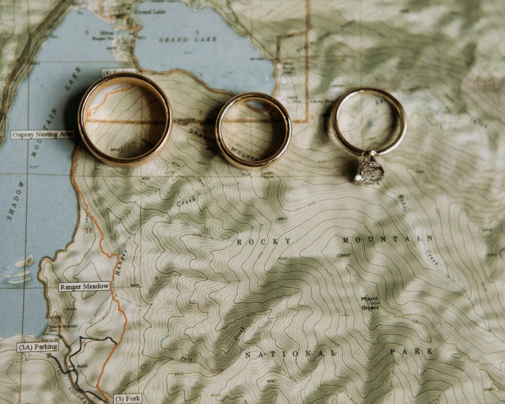 three wedding rings sitting on a map of rocky mountain national park