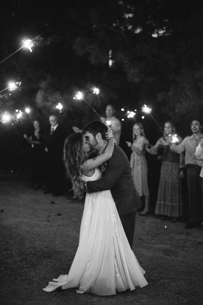 couple kissing during their elopement surrounded by family and friends holding sparklers