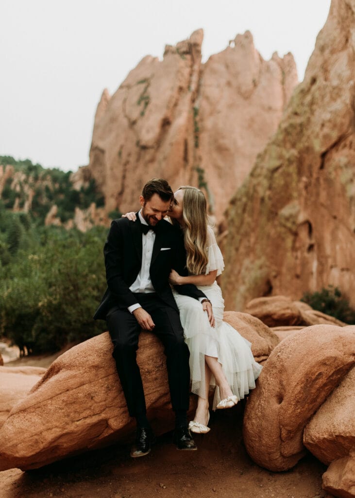 One of the best places to elope in Colorado is Garden of the Gods. A bride and groom sit on one of the amazing, unique red rocks in Colorado Springs.