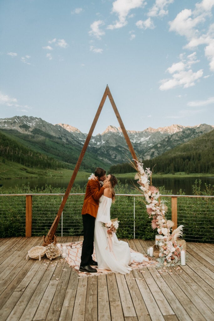 A couple kisses underneath their wedding arch at Piney River Ranch in Vail Colorado, One of the best micro wedding venues in Colorado