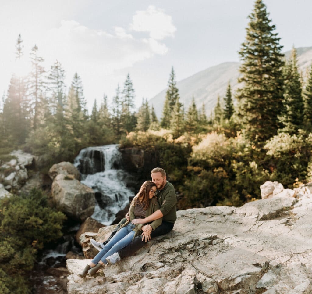 A couple snuggles up in front of a waterfall in Breckenridge, Colorado, one of the best elopement ideas for the couple that loves water.