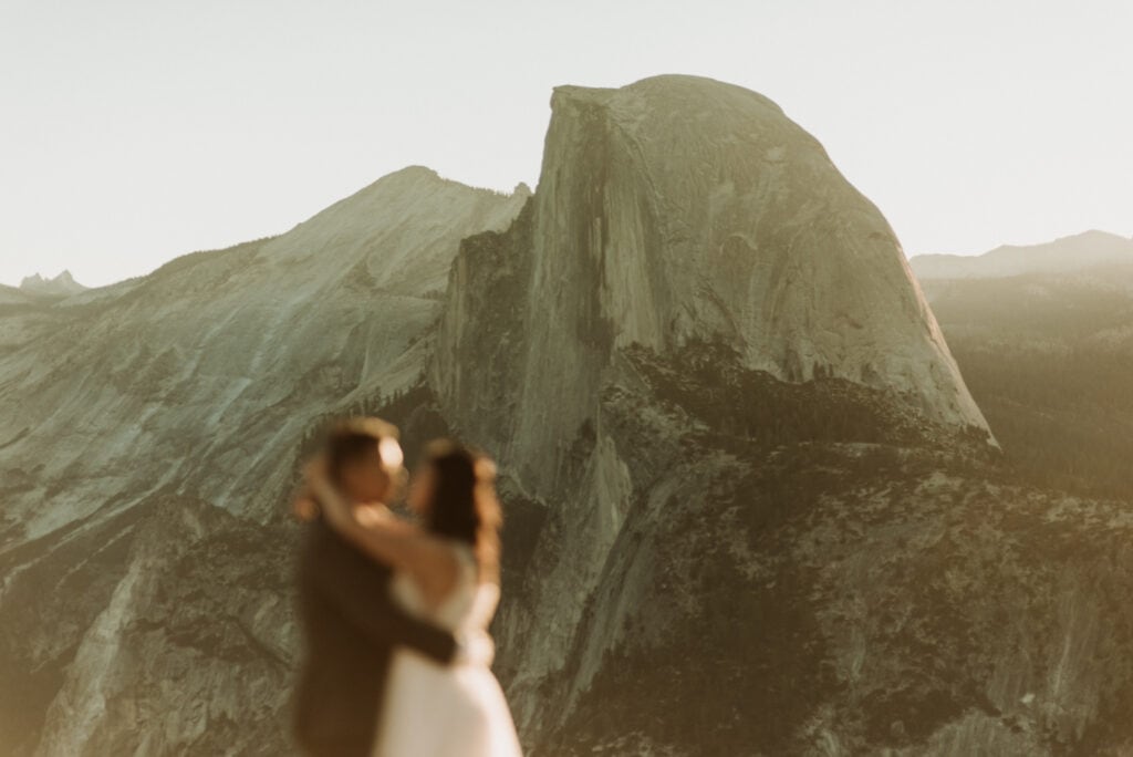 a couple hugging in front of half dome at glacier point on their yosemite elopement day