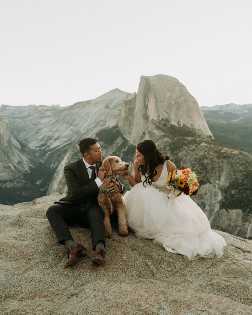 A couple snuggles their dog in front of Half Dome during their elopement in Yosemite National Park
