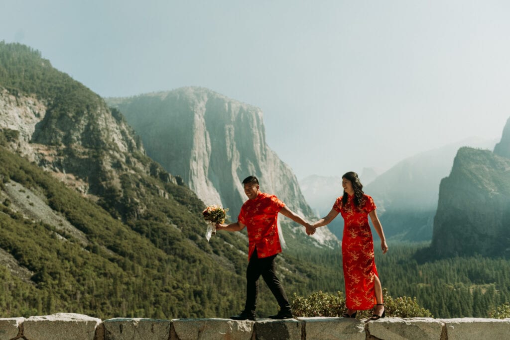 A couple walks along the edge of rocks at Tunnel View in Yosemite National Park during their elopement