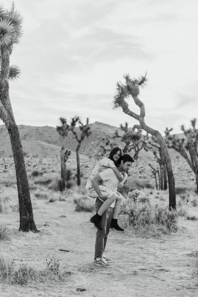 A woman getting a piggy back ride from her husband during their anniversary session in Joshua Tree california. Joshua tree national park engagement photos at cap rock