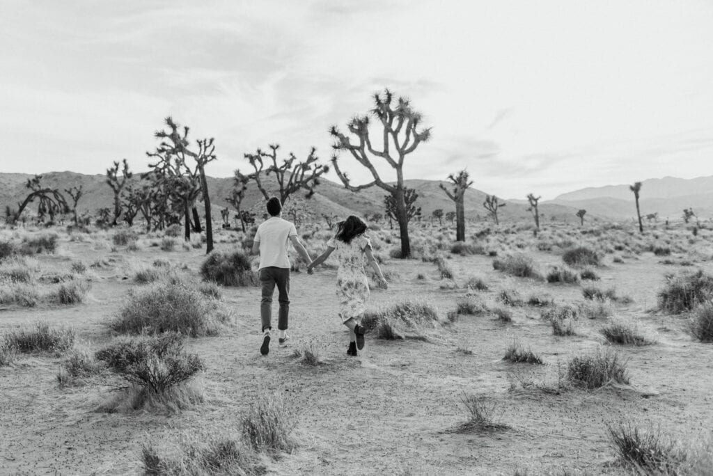 A couple running around in the desert for their anniversary session in Joshua Tree california. Joshua tree national park engagement photos at cap rock