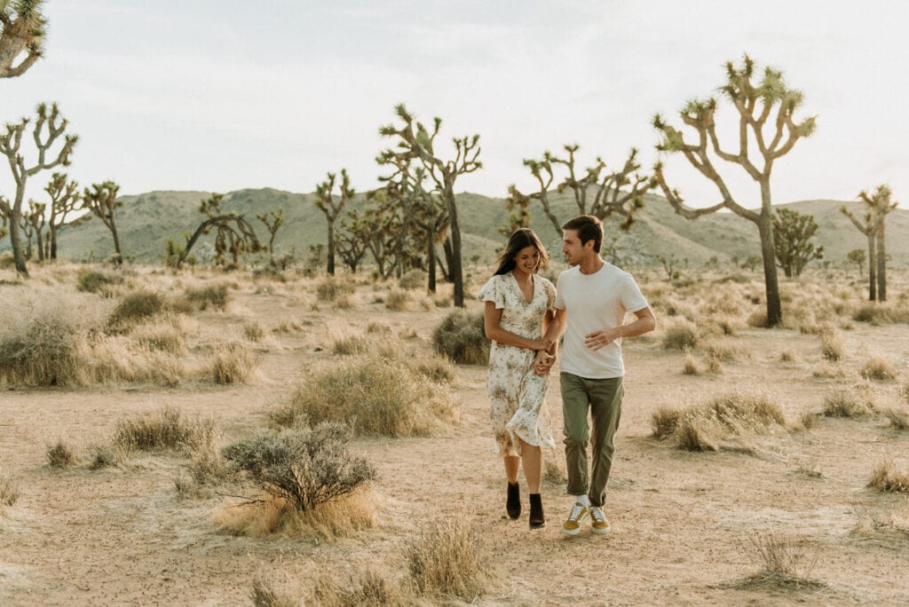 A couple running towards the camera in the desert for their anniversary session in Joshua Tree california. Joshua tree national park engagement photos at cap rock