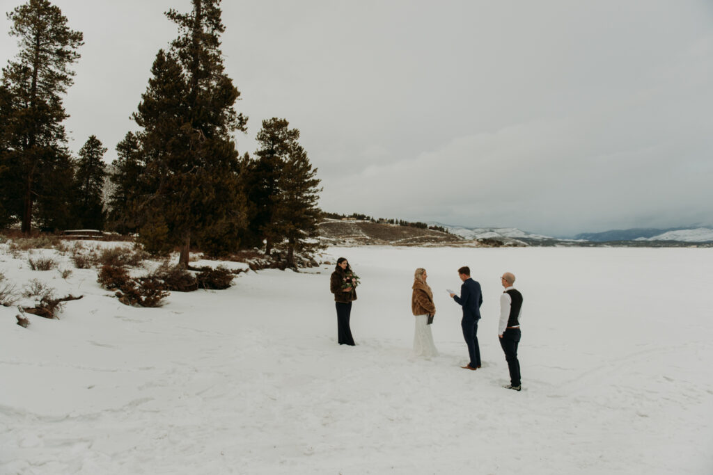 groom reading vows to bride at a snowy winter elopement in the mountains with family member present