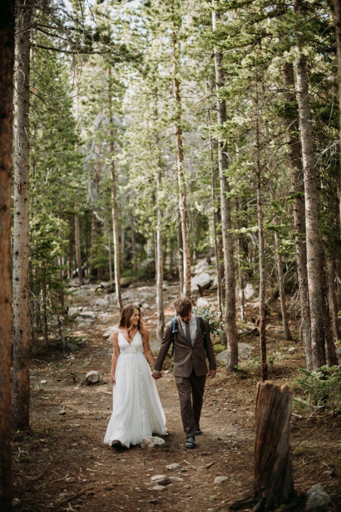 A wedding couple hiking through the forest of the venue Rocky Mountain National Park during their micro wedding