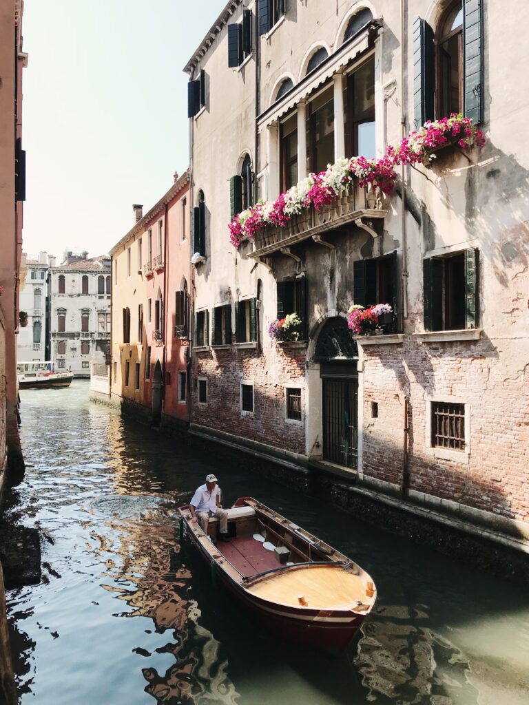 a gentleman sits on a boat steering through the canals of venice italy. How to elope in venice, italy