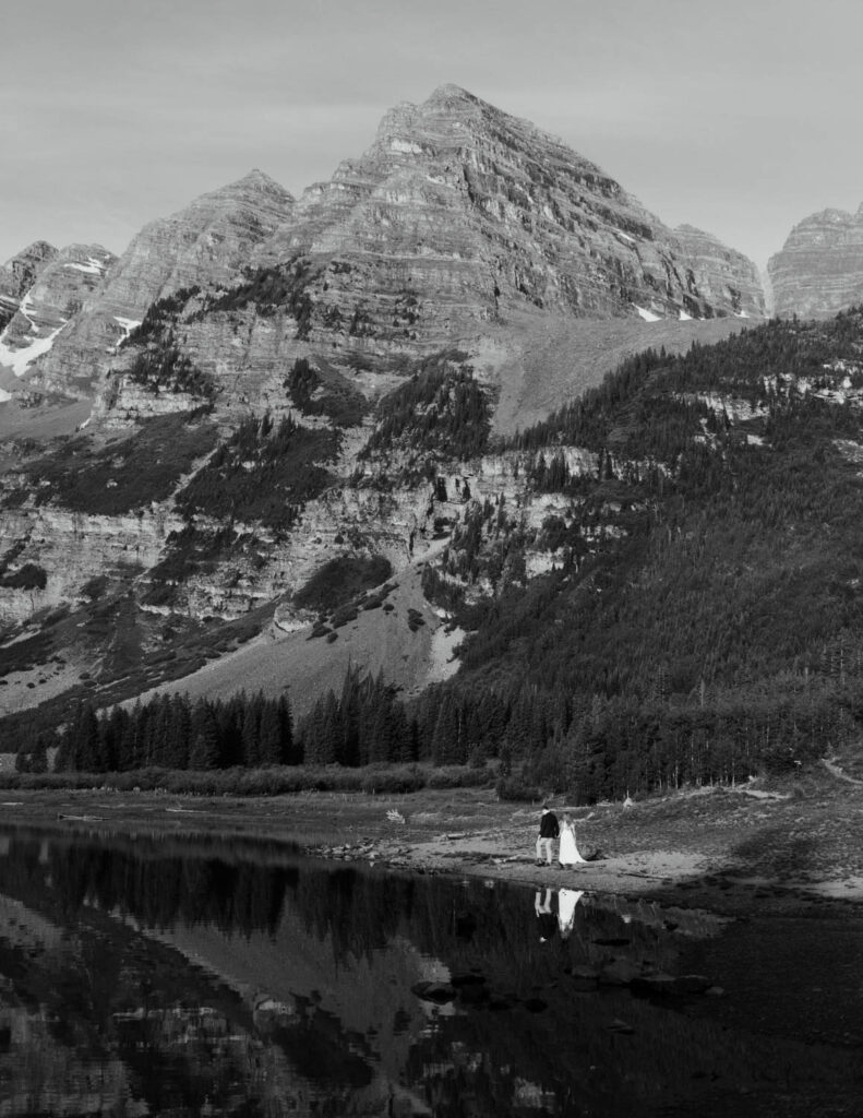 couple in wedding attire walking around the edge of an alpine lake at sunrise at maroon bells in aspen colorado. colorado elopement photographer