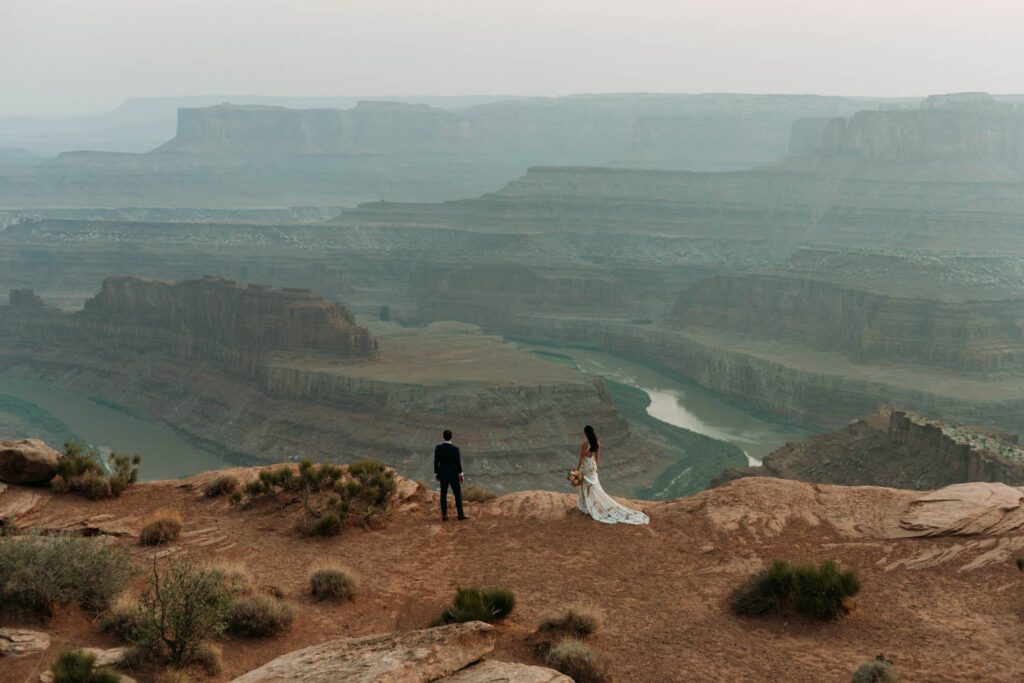 A couple stands looking out over the edge of a cliff in Dead Horse Point State Park, Moab, Utah on their elopement day. This is one of the best places to elope.