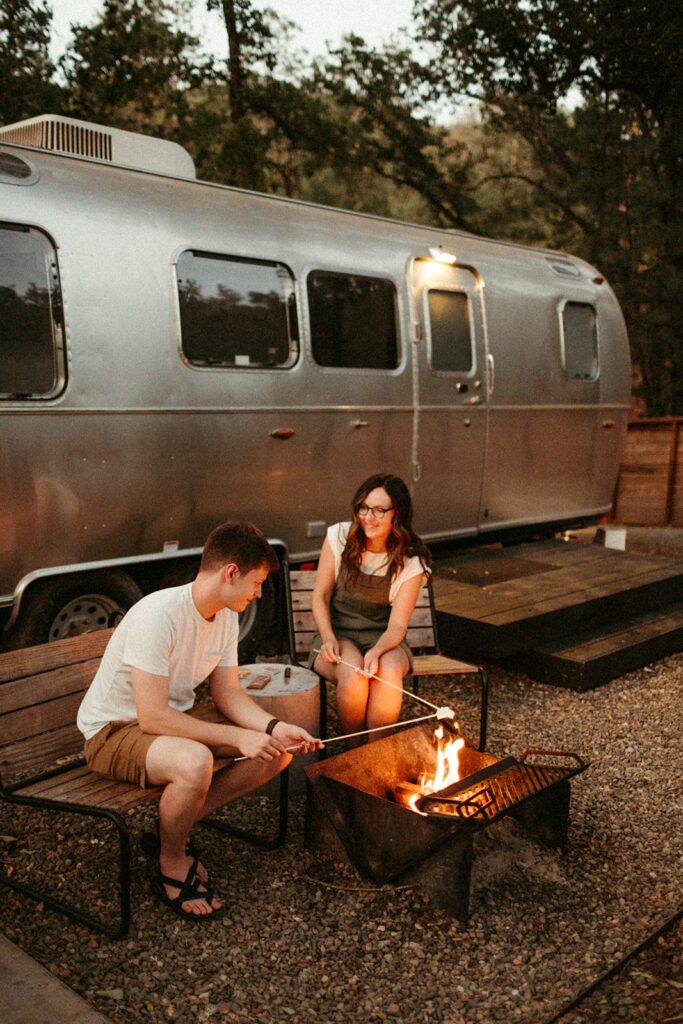 A couple roasts smores at twilight in front of a retro airstream at the micro wedding venue Autocamp Yosemite