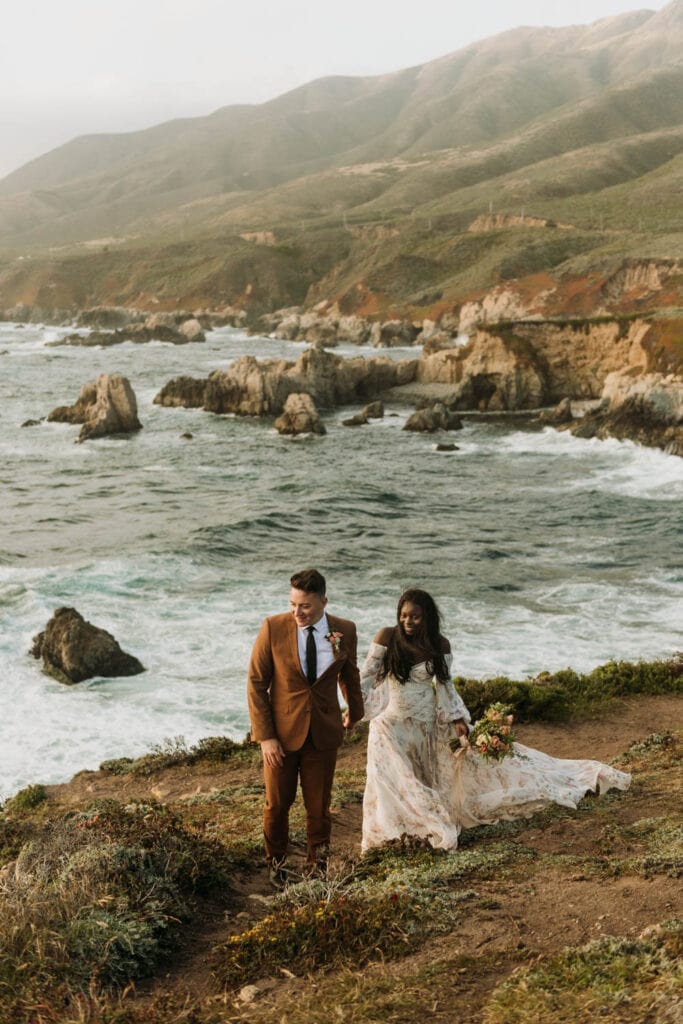 The best place to elope in Big Sur is Garrapata State Park along highway 1, a bride and a groom walk along the edge of a cliff overlooking the Pacific Ocean on their elopement day.