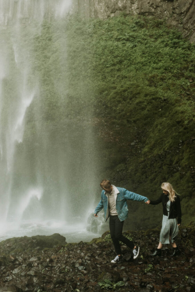 A couple walks underneath Latourell Falls in the Columbia River Gorge of Oregon, one of the best waterfall locations for an elopement!