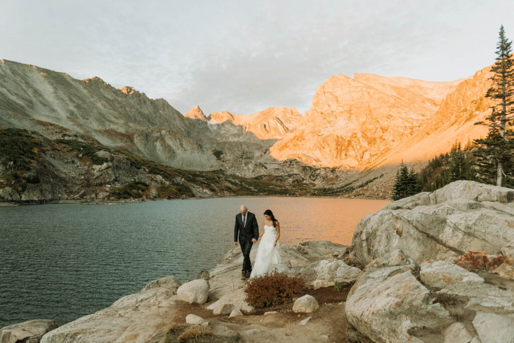 walking along the edge of Lake Isabelle, a couple holds hands during their elopement