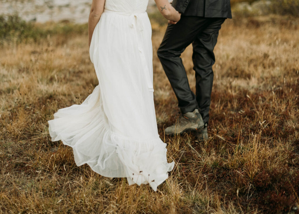 a couple holds hands and walks away through the meadow