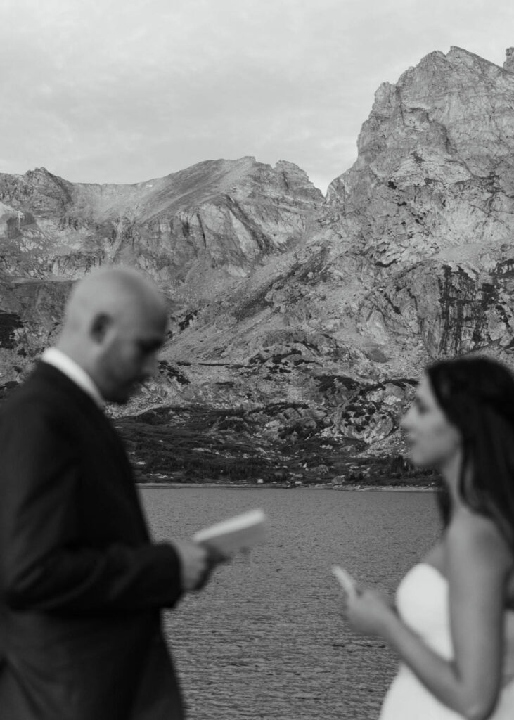 A couple reads their vows to each other at sunrise in front of Lake Isabelle during their elopement