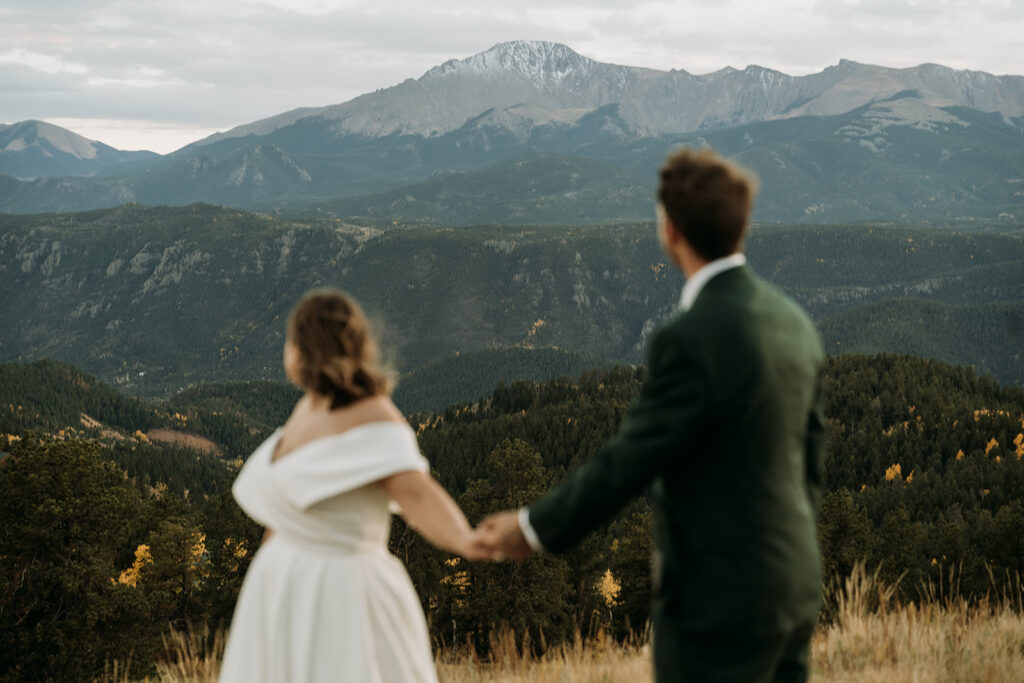 A couple holds hands walking with a view of Pikes Peak during their Colorado Springs Elopement