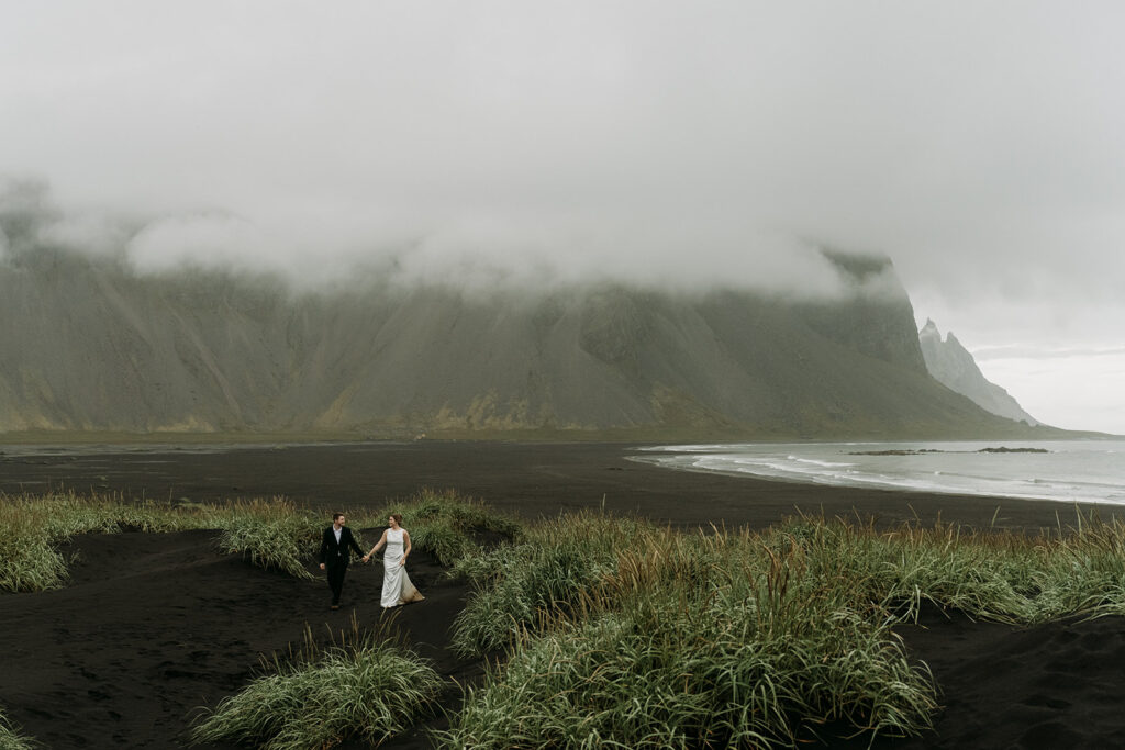 Couple walking on a black sand beach during their Iceland elopement at Stokksnes