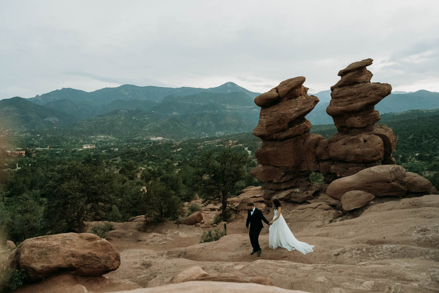 A couple walks hand in hand in front of Siamese Twins at Garden of the Gods during their micro wedding