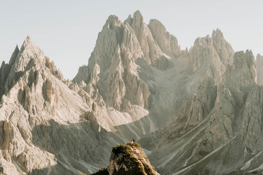 A couple stands on a ledge overlooking jagged mountain peaks during their cadini di misurina dolomites elopement in italy