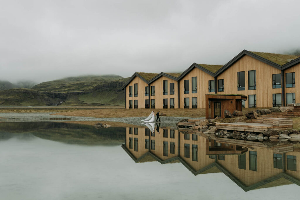 A wedding couple walks along the shoreline in front of Hotel Jokulsarlon where they got ready for their Stokksnes elopement