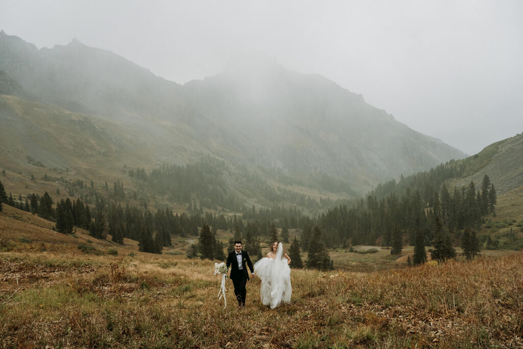 A couple running through an alpine meadow during their fall aspen elopement